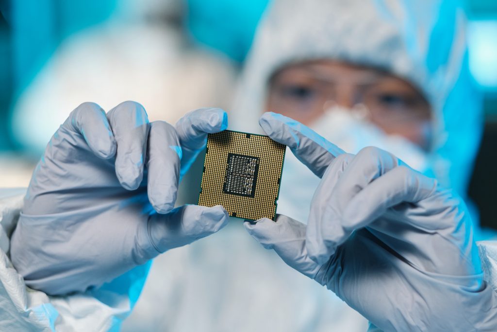 Gloved hands of a scientist holding a microchip in a cleanroom environment